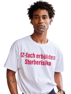 Ein Mann, der ein weisses T-Shirt mit der Aufschrift „12-fach erhöhtes Sterberisiko“ trägt.